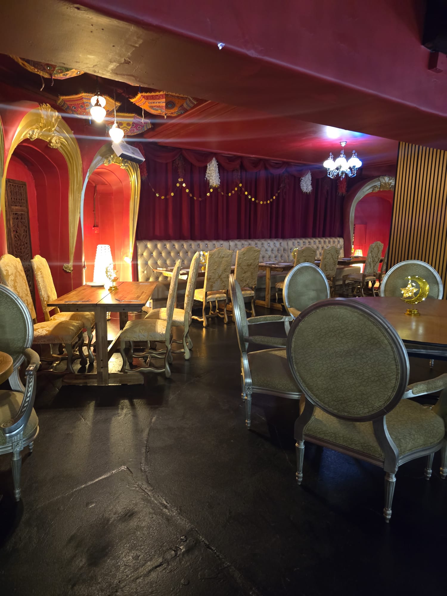 Intimate Mehndi setup at Opulent @ 35 Liverpool — deep red arched dining room with hanging Rajasthani parasols, gold chandeliers and carved chairs